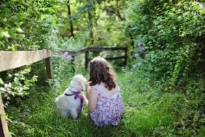 A girl sitting in a lush, green path, gently petting a white dog