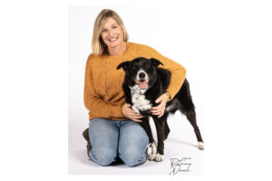 A smiling black and white dog sits beside a woman