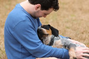 A man gently cradles his dog in a dry grassy field