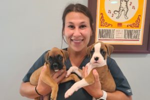 A woman smiles while holding two adorable puppie