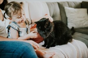 A woman and a child gently petting a black cat