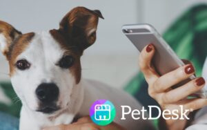 A person uses a smartphone beside a small dog, featuring PetDesk