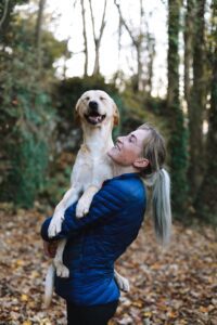 A happy yellow Labrador is being held by a person in a blue jacket