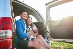 A man and woman sit in a car, smiling with their dog