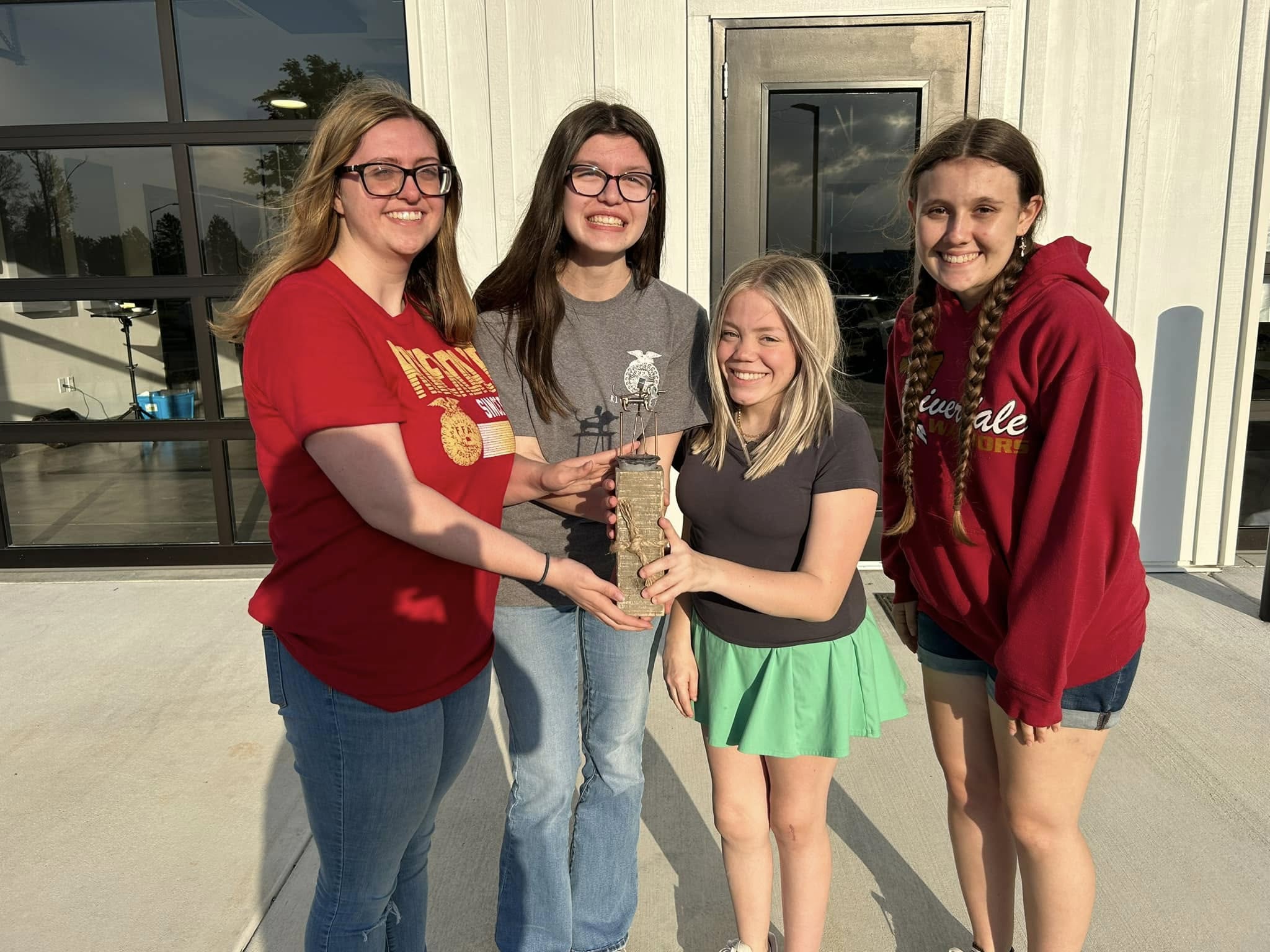 Four girls are smiling while holding a trophy together